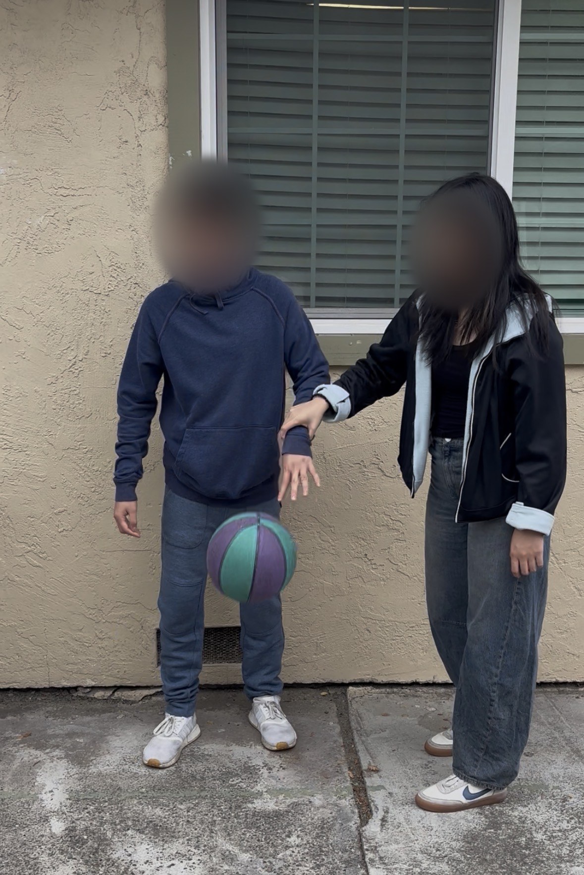 A HoopsInUnity session: the founder guides a student's arm as he drops a basketball. Both faces are blurred.